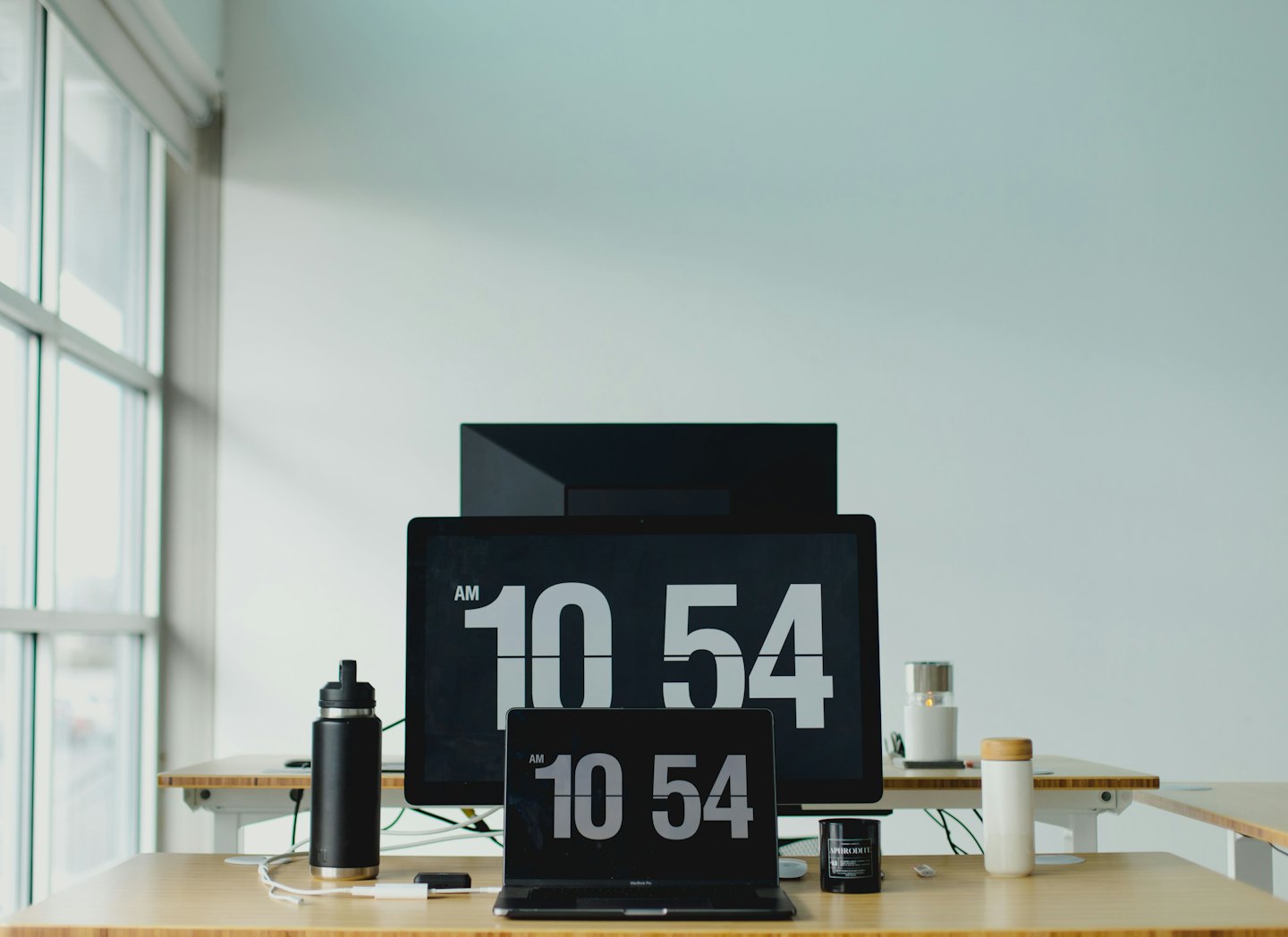 Modern standing desk with dual monitors displaying the time.