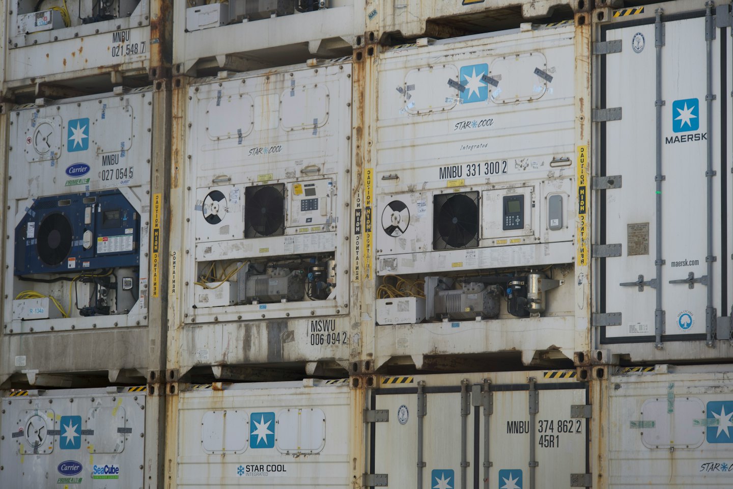 Weathered shipping containers stacked outdoors featuring industrial cooling units.